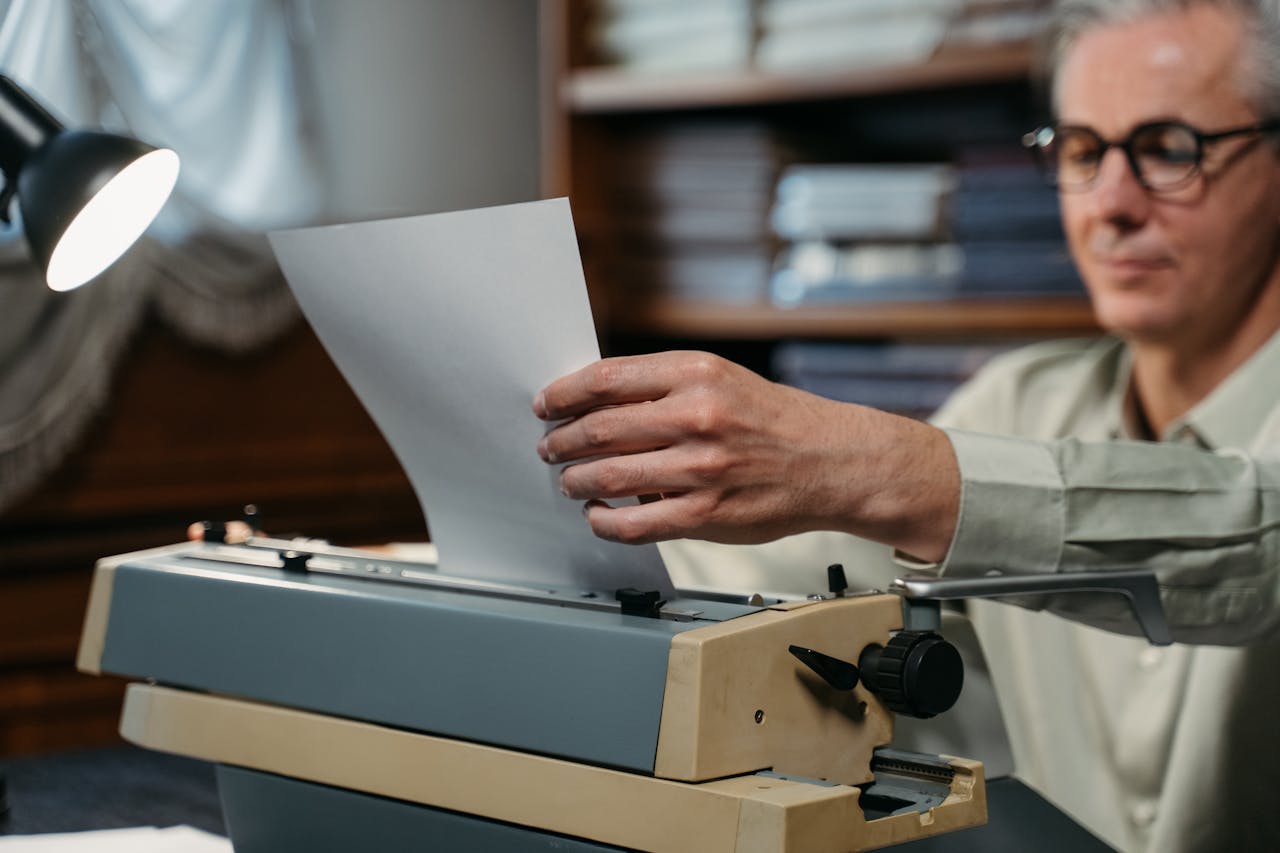 An elderly man typing on a vintage manual typewriter in a cozy indoor setting.
